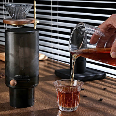 Person pouring coffee from a glass jug into a clear cup using a stylish coffee dripper.